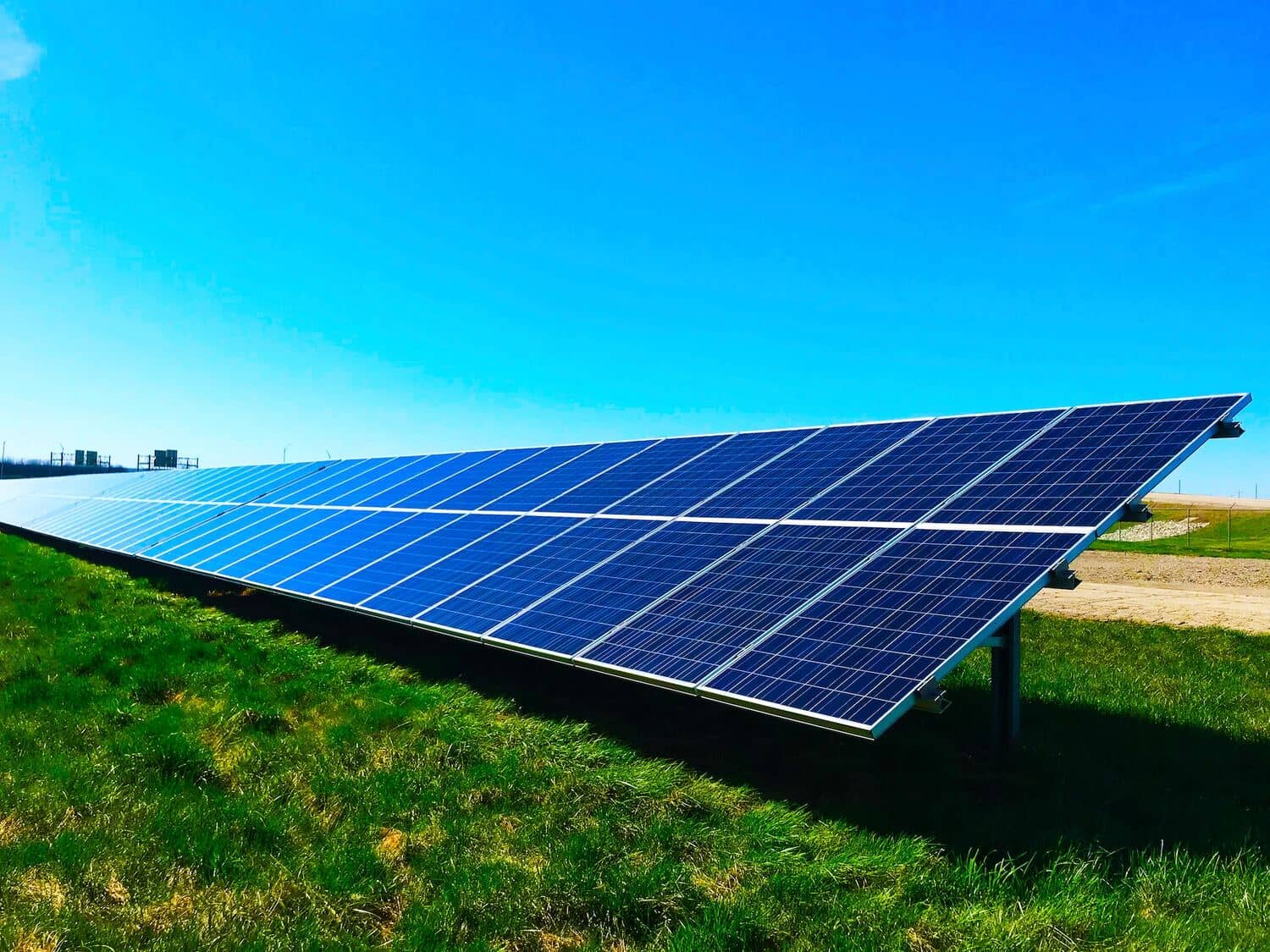 A large solar panel array is installed on a grassy field under a clear blue sky.
